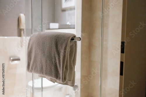 Soft white towel hanging on glass shower door in modern hotel bathroom interior