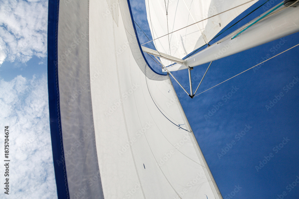 Fototapeta premium Blue and White Sailboat with Full Sails Against Sky