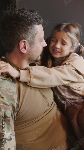Soldier smiles as daughter hugs him during family reunion at home after returning from deployment,vertical video