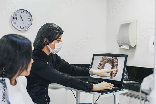 Dentist explaining dental images on a computer to a female patient during a routine consultation in a clean and modern dental clinic.