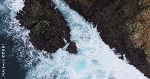 Top down aerial of Atlantic waves surging through a narrow rocky channel near Coruna, Galicia, Spain, powerful surf and white foam patterns