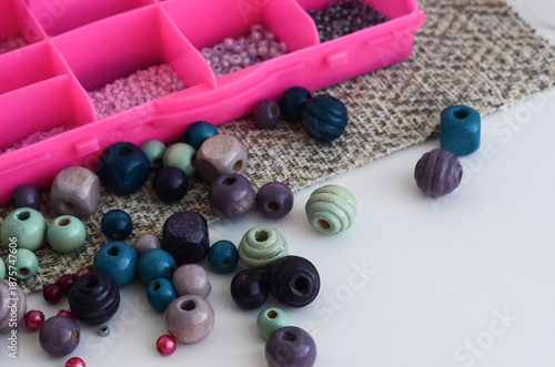 Multi-colored wooden beads lie on the table against the background of a box with beads. Creativity and needlework concept.