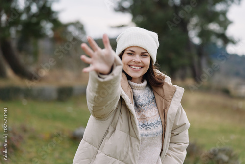 Foto Woman in a warm winter coat reaching out with a smile in an open park, cold weather, soft natural light, candid portrait conveying friendliness and outdoor joy
