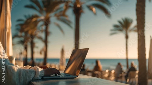 Ultra HD Person working on laptop at a beachside cafe with palm trees and ocean at sunset, embodying remote work and digital nomad lifestyle video