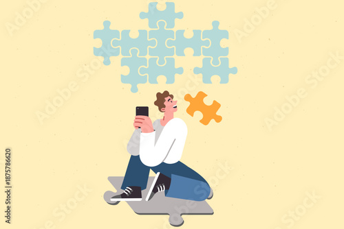 Teenager guy with phone playing application with logic game, putting puzzle cubes together