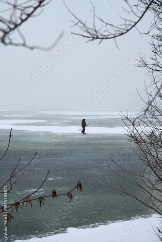 A lone fisherman walks along a frozen river to catch fish under the ice