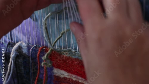 Close-up top view of artist hands weaving colorful tapestry on a loom. The artisan meticulously knots threads to create unique handmade textile wall art design.

