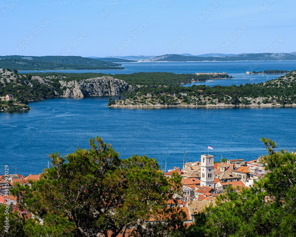 Obraz premium A high-angle view overlooking the red roofs of Šibenik town, the blue bay, and the many islands of the Dalmatian coast