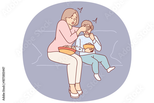 Shocked mother closes son eyes while watching television show with scenes of violence