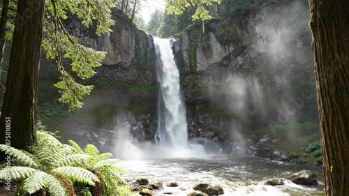 Majestic tall waterfall plunges powerfully into a rocky pool surrounded by lush green temperate rainforest foliage and towering ancient trees.