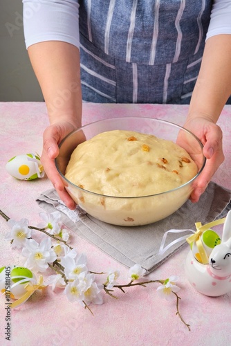 Step by step preparation of Easter cake or other Easter pastry on pink concrete background. Ready fermented dough with raisins in glass bowl. Happy Easter.