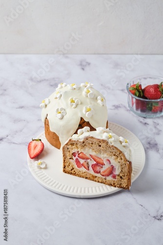 Sliced ​​cake filled with custard and strawberries covered with white icing and decorated with marshmallow flowers on a light background. Desserts strawberries.