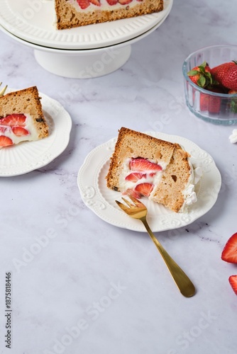 Sliced ​​cake filled with custard and strawberries covered with white icing and decorated with marshmallow flowers on a white plate on a light background. Desserts strawberries.