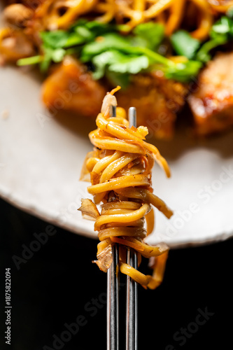 Fotografie close-up shot of stir-fried noodles, possibly chow mein, wrapped around a fork, with the main dish blurred in the background