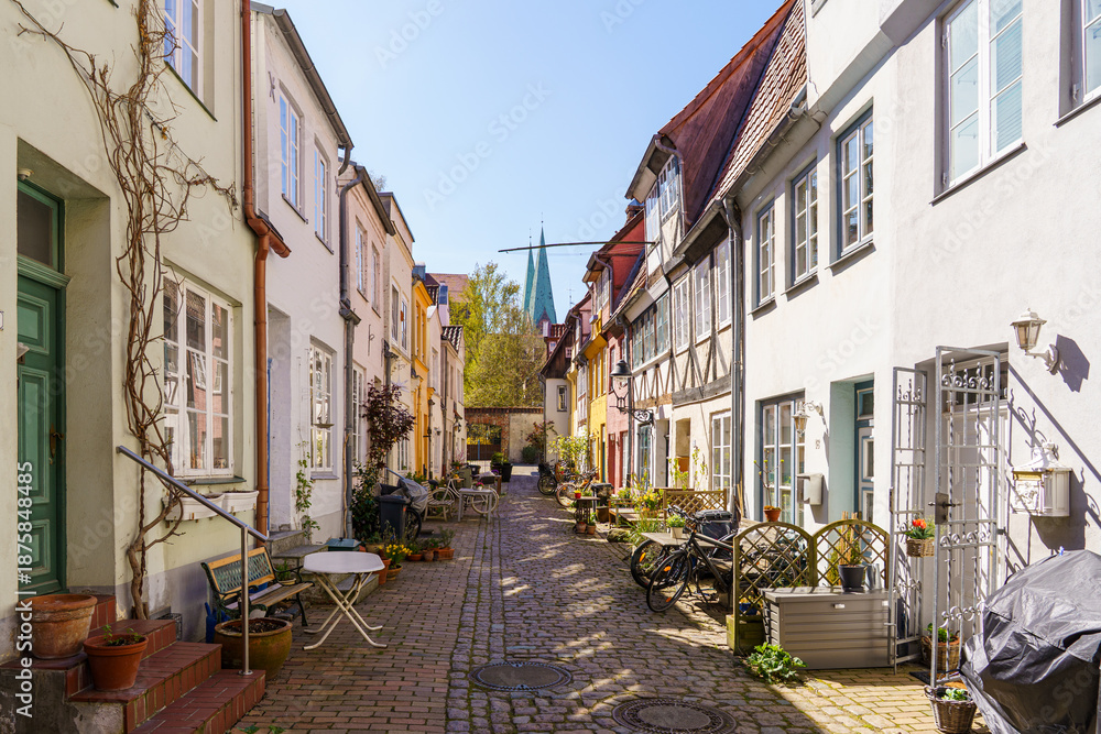 Ταπετσαρία A narrow cobblestone street in Lubeck Germany with a row of houses and a church in the background
