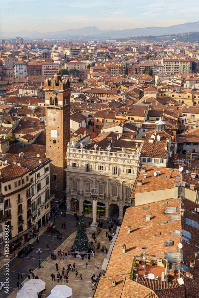 Naklejka premium A panoramic view of the city of Verona, Italy, from above. A tall, square, red brick tower is visible in the center of the image The Alpine mountains are visible in the background