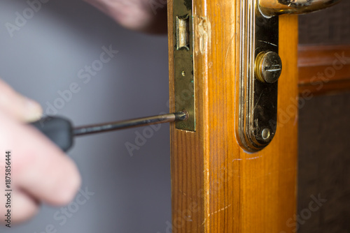 Fotografie Skilled technician using a screwdriver to repair a wooden door lock, showcasing