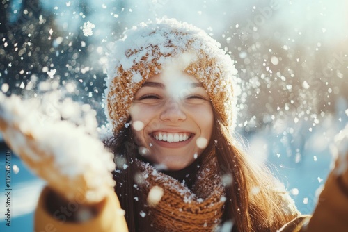 A woman wearing a hat and scarf is smiling broadly as she embraces the falling snowflakes. She appears happy and excited by the winter weather.