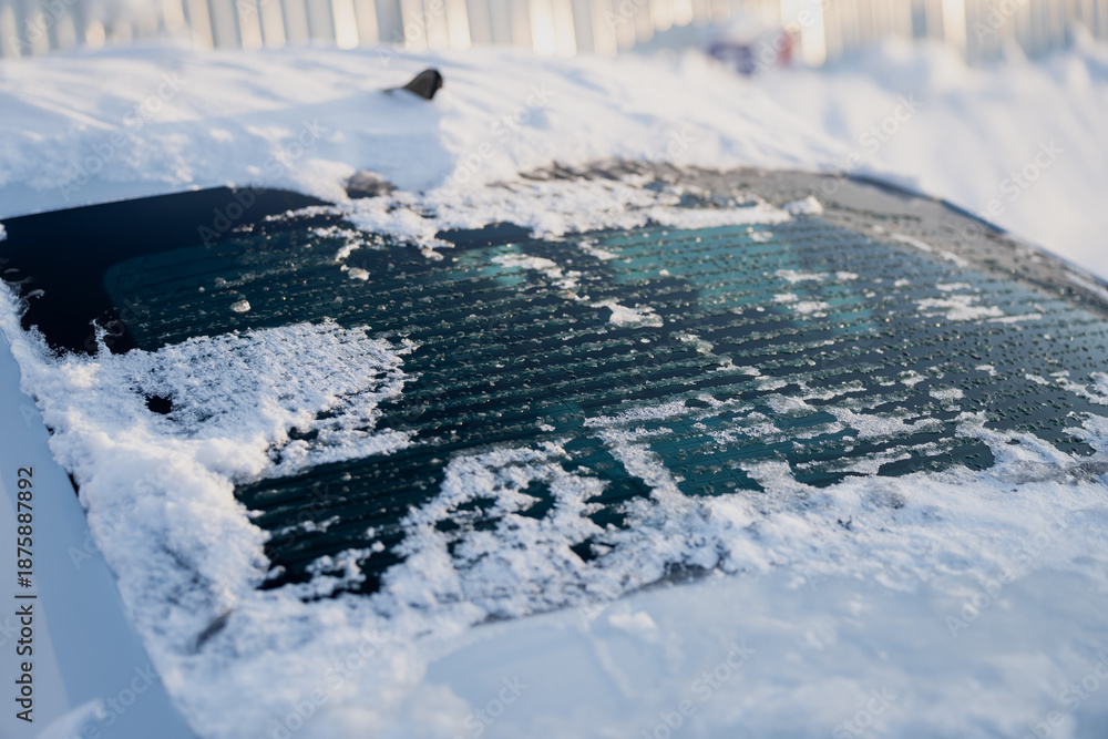 Obraz premium Rear car window with snow buildup and thawing ice, detailed defroster stripes and droplets on glass surface, close up automotive winter conditions scene