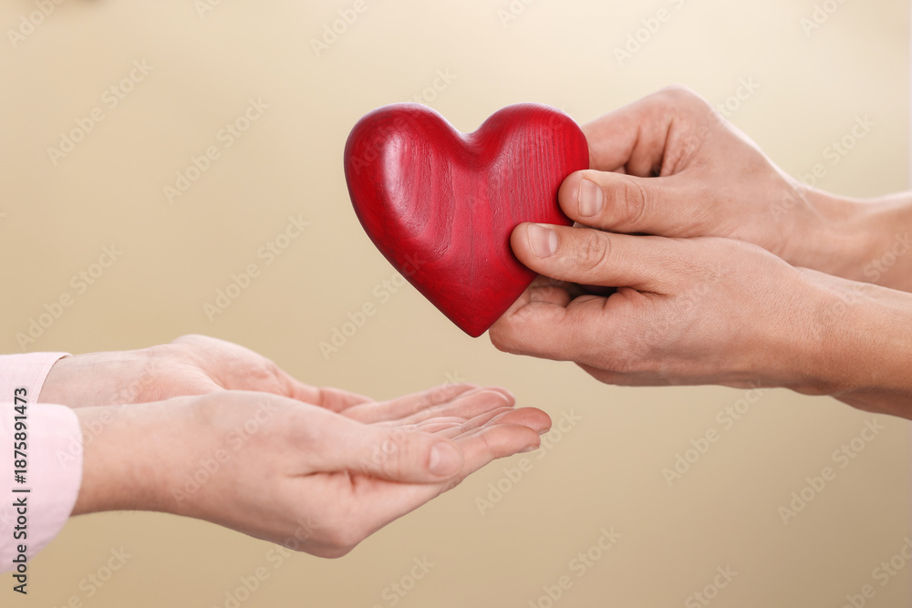 Obraz premium Man giving red decorative heart to woman on beige background, closeup