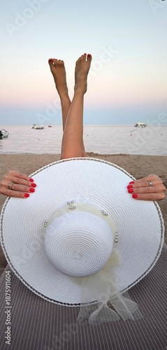 The epitome of summer serenity, a girl in a hat on the beach with her legs raised to the sky