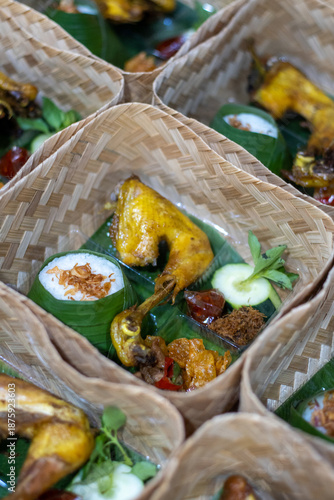 Traditional Indonesian food served in woven bamboo baskets with banana leaf, turmeric chicken, rice, and side dishes. Sustainable catering, authentic Asian cuisine concept