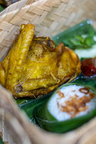 Close-up of Indonesian turmeric chicken served with rice wrapped in banana leaf inside a woven bamboo basket. Traditional Asian food with authentic and rustic presentation
