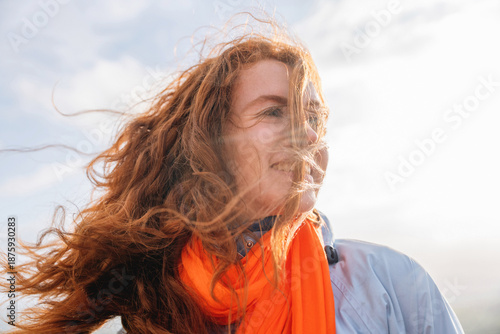 Cuadro en lienzo Redhead Woman with long hair smiling against cloudy sky while wearing orange sca