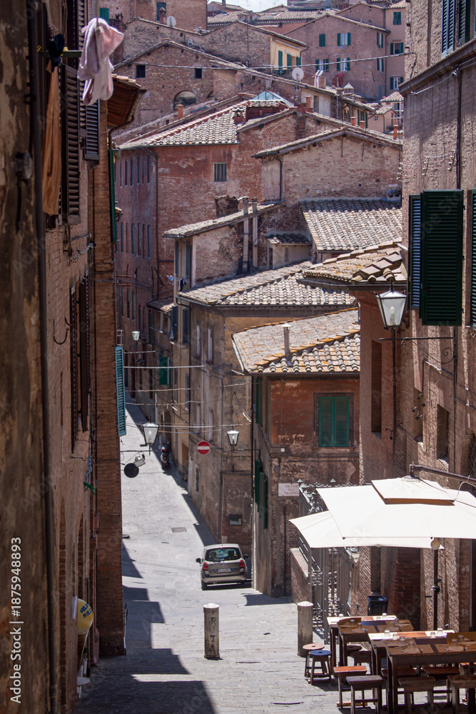 Obraz premium Historic alleyway in Siena featuring traditional brick houses, shuttered windows, and classic Tuscan urban character. Captured in soft daylight with strong architectural depth.