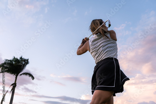 Photos A latin hispanic woman golfer in a sleeveless top makes a full swing with a golf