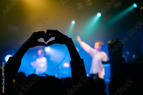 Картината върху платно Silhouette hands making heart shape at live concert with blue stage lights