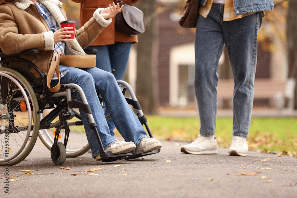 Obraz premium Young woman in wheelchair with coffee and her friends on street