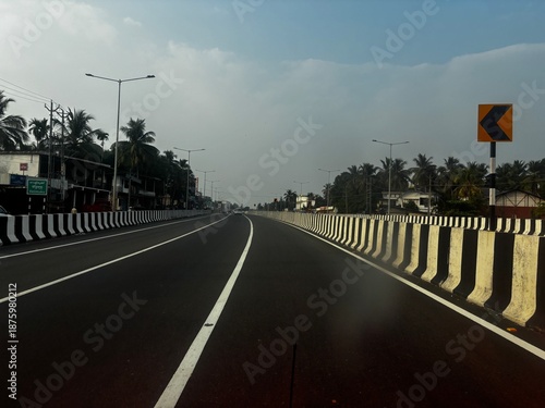 Photo of a newly constructed road in Kerala, India, showcasing smooth asphalt surface, fresh road markings, and well-planned infrastructure. Surrounded by greenery, coconut trees, and a tropical lands
