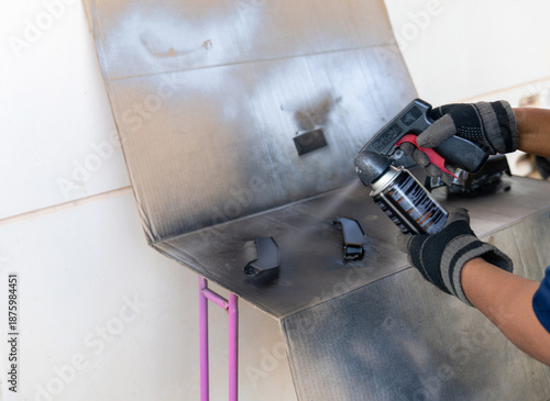 Εκτύπωση καμβά A person wearing protective gloves using a black aerosol spray paint can with a trigger handle attachment to restore motorcycle parts