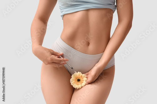Canvas-taulu Young woman in panties with flower and syringe on light background, closeup
