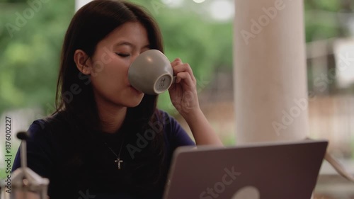 4K video of young happy asian woman working on laptop at home while drinking coffee in the morning. Female student learning online. Education or business concept.