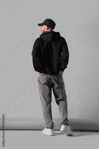 Young man in black hoodie with cap on grey background, back view