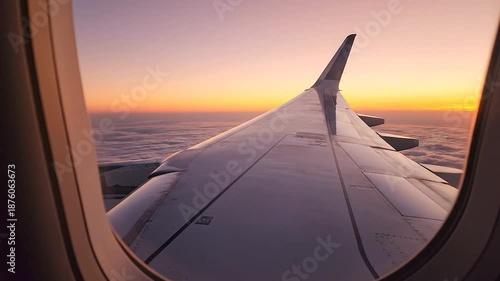 Airplane wing above clouds, framed by window, illuminated by a stunning gradient sunset