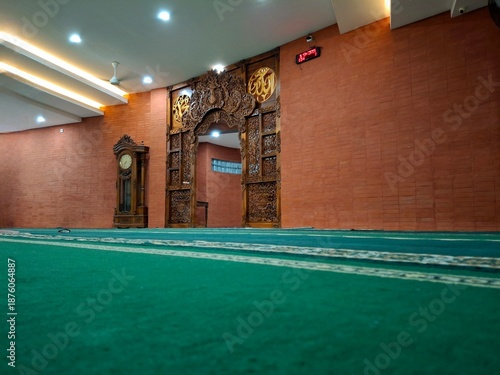 Modern mosque interior featuring traditional Javanese wood carvings and green prayer carpet. Ideal for Islamic religious themes, Ramadan, and cultural architecture backgrounds.