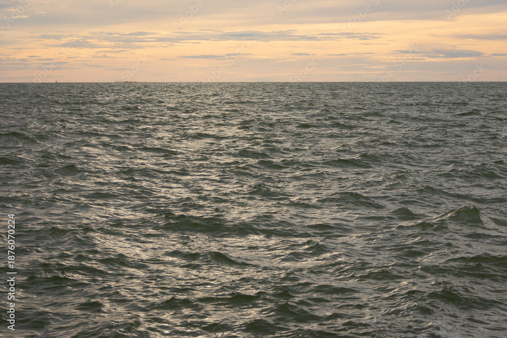 Fototapeta premium A wide shot of the ocean surface under a sky with soft clouds and a warm