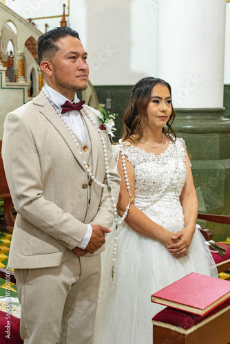 Traditional Hispanic wedding ceremony in a Catholic church with a young bride and groom standing at the altar.