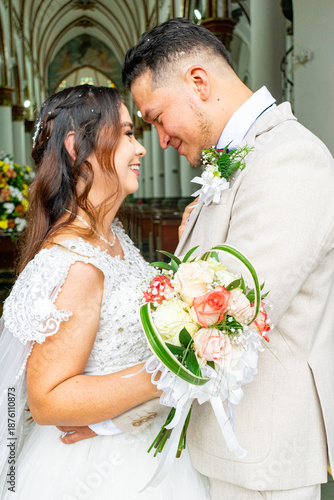 Romantic portrait of a happy young Hispanic bride and groom looking at each other with love during their wedding ceremony in a traditional church.
