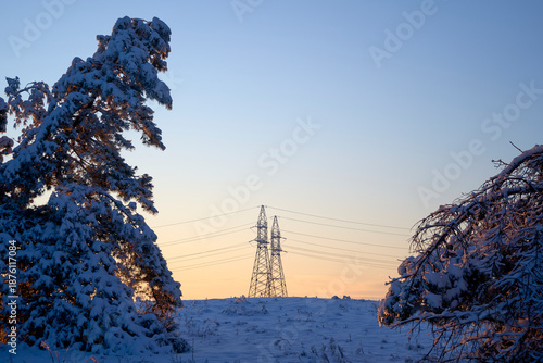 High voltage power line pole between snow covered trees in winter.Background on the theme of energy and transmission of electricity over long distances in difficult conditions,in a cold,snowy climate