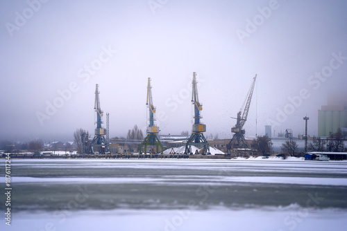 Blurred silhouettes of cranes in the river port against the background of winter fog