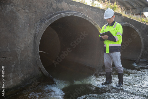 Bild auf Leinwand A male water resources engineer is standing and working in front of a drainage pipe