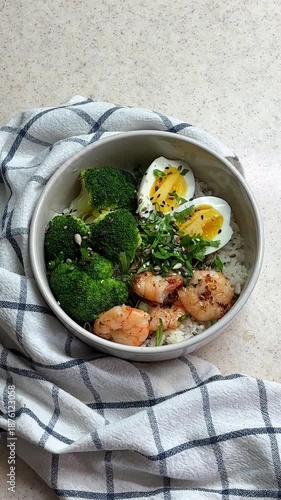 Homemade poke bowl with shrimps, rice and vegetables. Healthy bowl with prawns, broccoli, edamame beans, eggs and Chuka Wakame seaweed. Sprinkle with sesame seeds