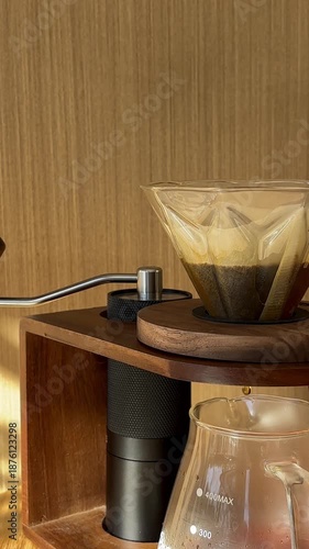 Close-up of pouring water from black kettle in v60 paper filter with fresh grind coffee beans on the wooden table in cafe or at home