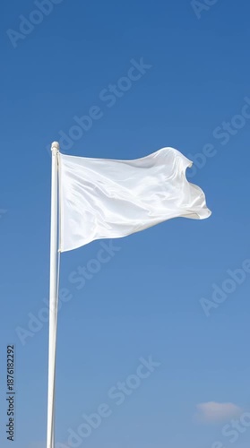 A blank white flag on a flagpole waving gently in the wind against a clear, vibrant blue sky. Vertical video ideal for social media. A symbol of peace, truce, surrender or a new beginning