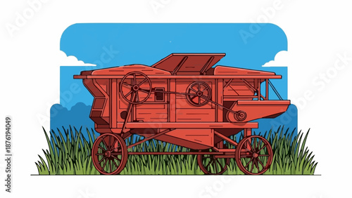 Red antique thresher machine stands in tall green grass under a blue sky