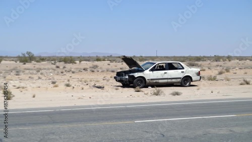 Broken down vehicle on roadside with open hood in desert landscape